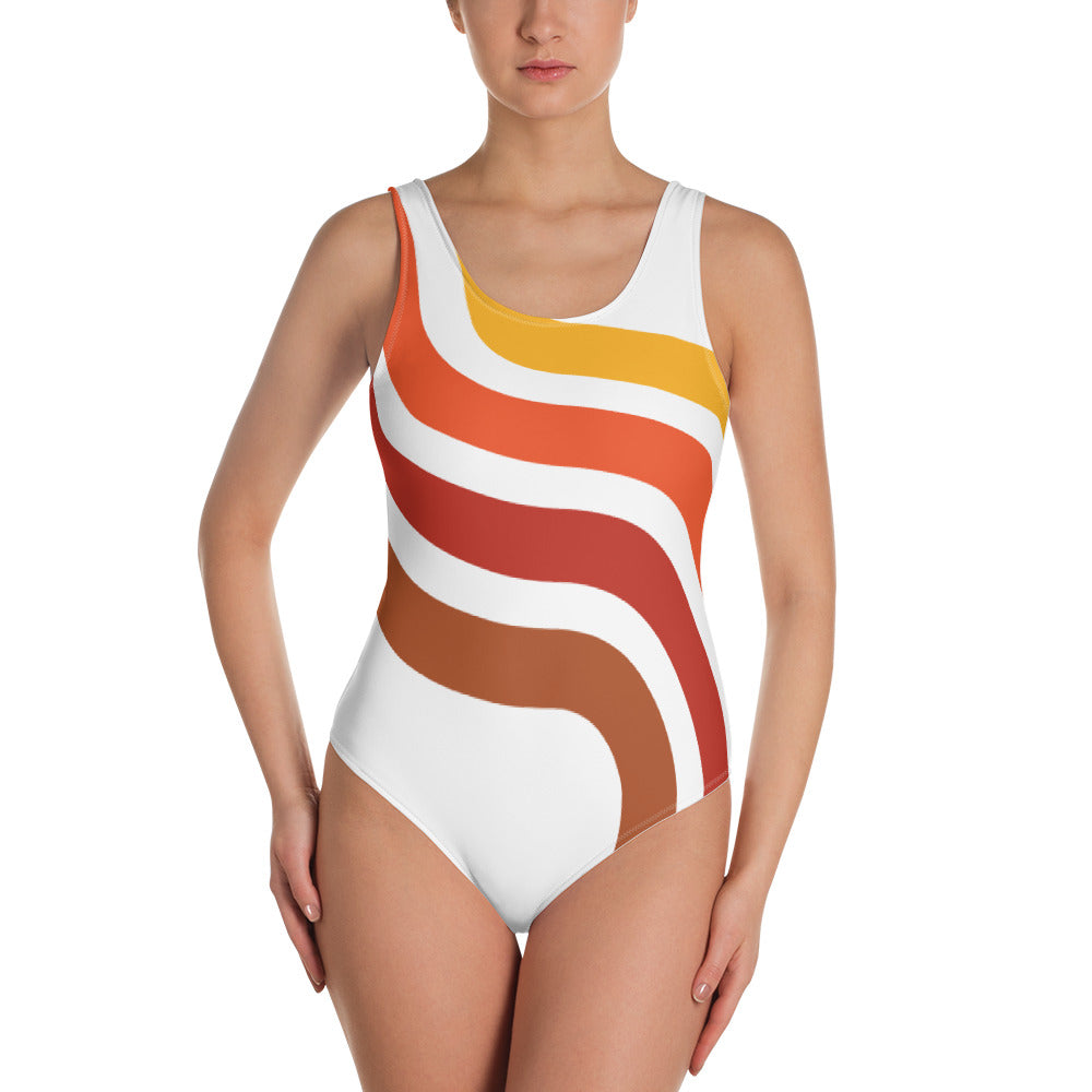 La fiche produit présente une femme en maillot de bain blanc avec un motif de courbes orangées allant du côté haut gauche jusqu'au bas de la hanche droite. Ce maillot de bain offre un look vintage et tendance, avec une coupe flatteuse pour la silhouette. La vue de face permet de voir en détail le motif et la couleur du maillot. Cette description est également adaptée pour les clients malvoyants afin qu'ils puissent se faire une idée précise du produit.